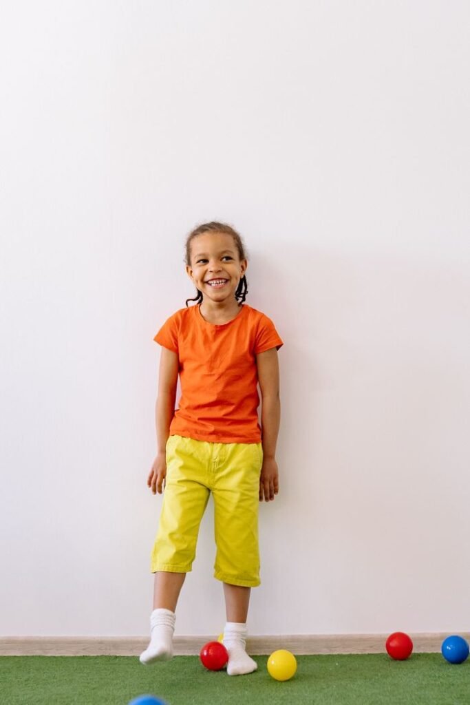 Smiling child in a bright outfit playing with balls indoors, expressing joy and carefree fun.